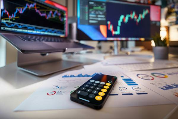 desk showing a price chart on a desktop screen and a calculator app on a phone